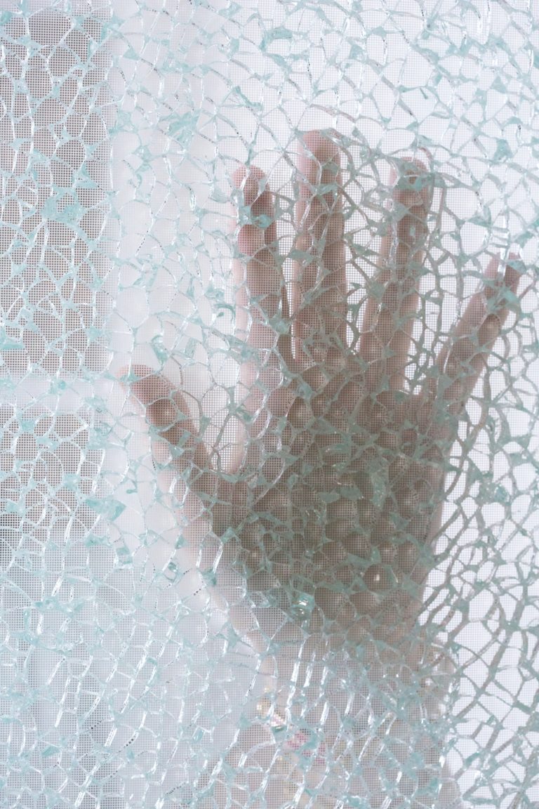 Hand berührt von hinten eine zersplitterte Glasscheibe