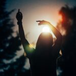 Silhouette einer tanzenden Frau vor Sonne und Bäumen