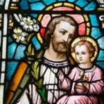 Kirchenfenster, das einen weissen Mann mit Bart zeigt, der auf seinem Schoss ein etwa vierjähriges Kind trägt. Beide haben einen Heiligenschein.