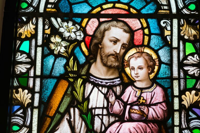 Kirchenfenster, das einen weissen Mann mit Bart zeigt, der auf seinem Schoss ein etwa vierjähriges Kind trägt. Beide haben einen Heiligenschein.