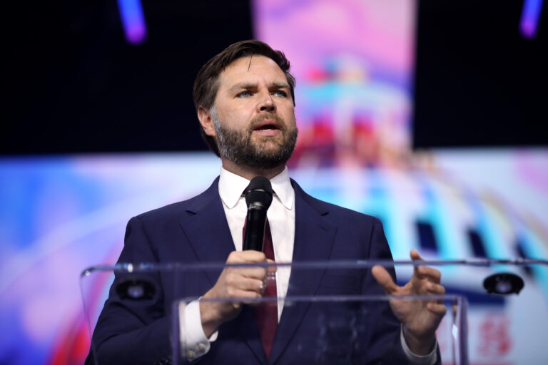 JD Vance, weisser Mann mit schwarzem Anzug, hält ernst dreinblickend Vortrag