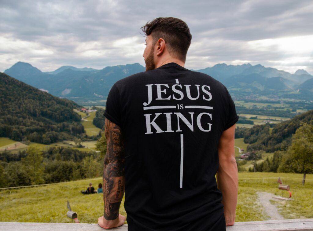 Mann mit T-Shirt "Jesus is King" vor Berglandschaft