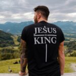 Mann mit T-Shirt "Jesus is King" vor Berglandschaft